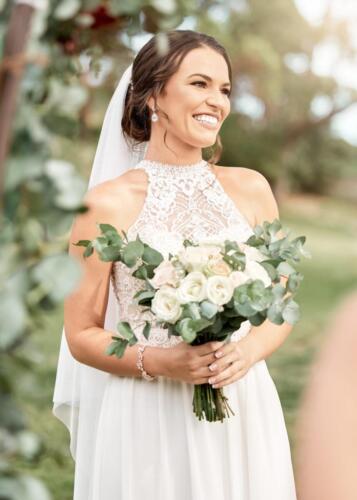 Bride in white gown, with flowers and happy at her spring wedding. Woman in wedding dress with bouquet of roses in her hands, smile and pose on day of her marriage ceremony in garden